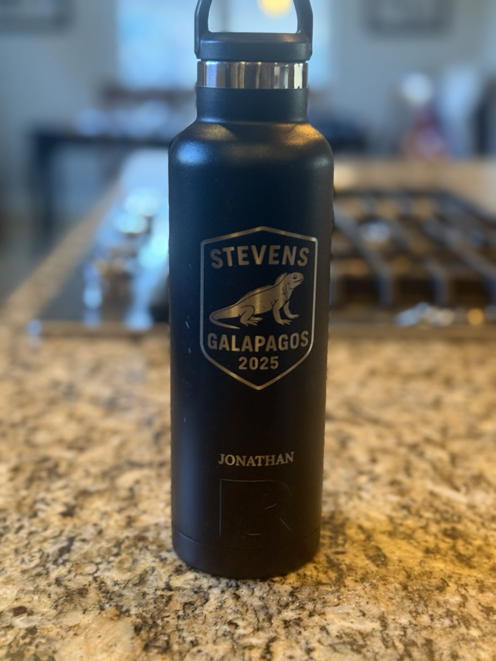 A black RTIC water bottle engraved with a shield badge reading Stevens, Galapagos 2025, with an iguana, and the name Jonathan
