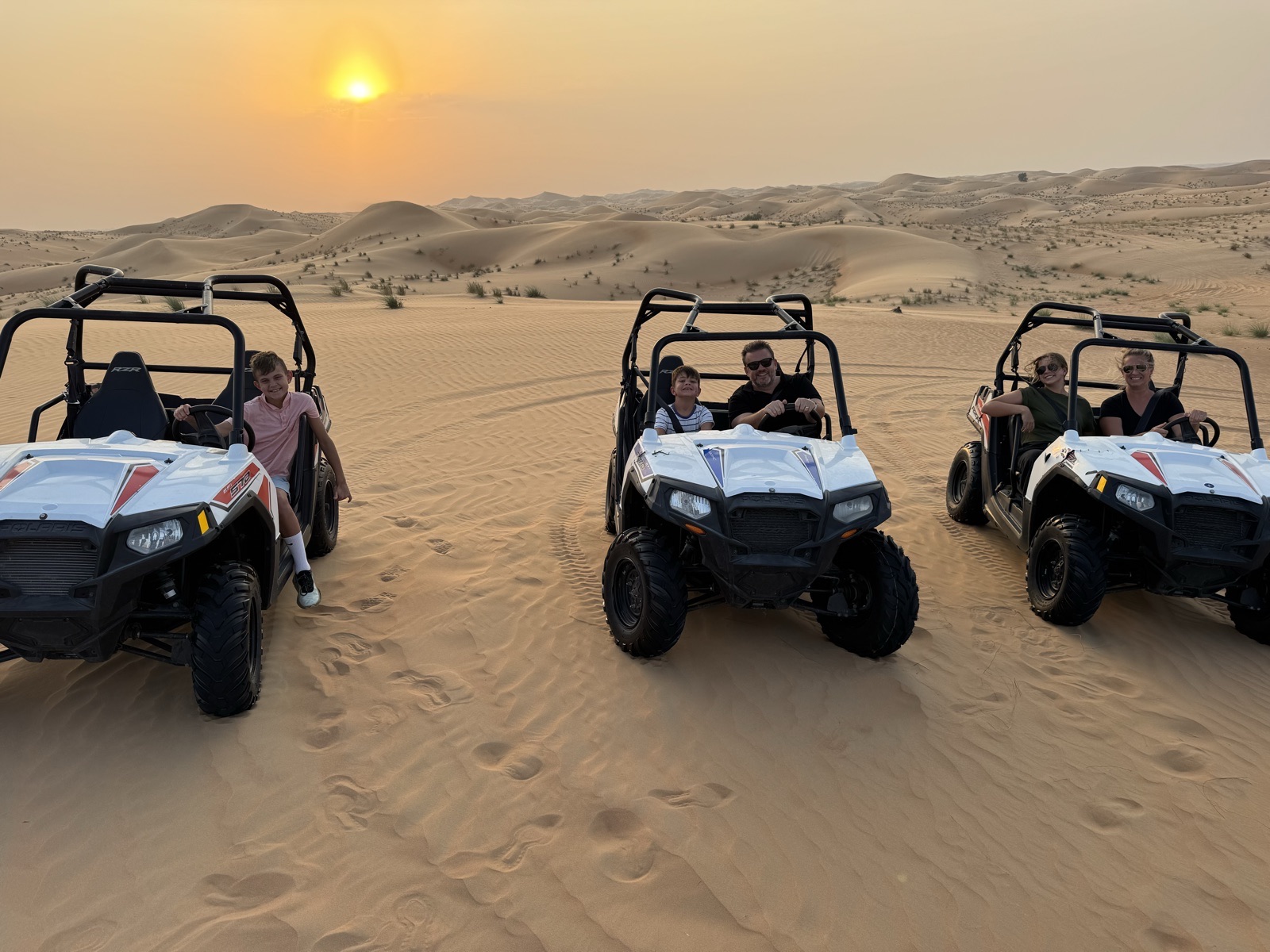Three dune buggies on the sand at sunset in the Abu Dhabi desert